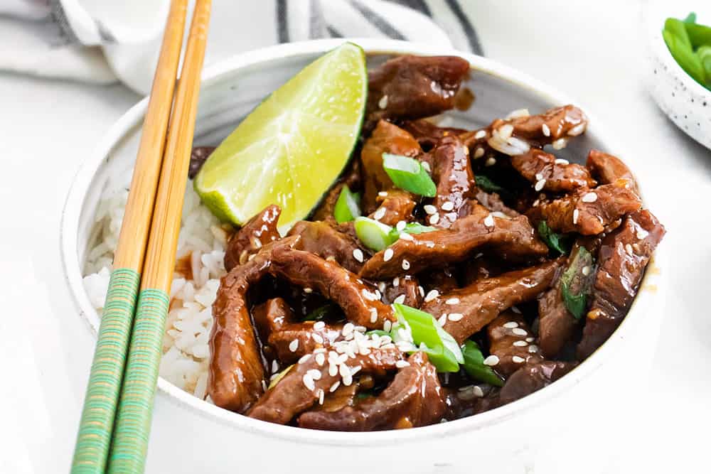 bowl of sesame beef with white rice topped with chopsticks