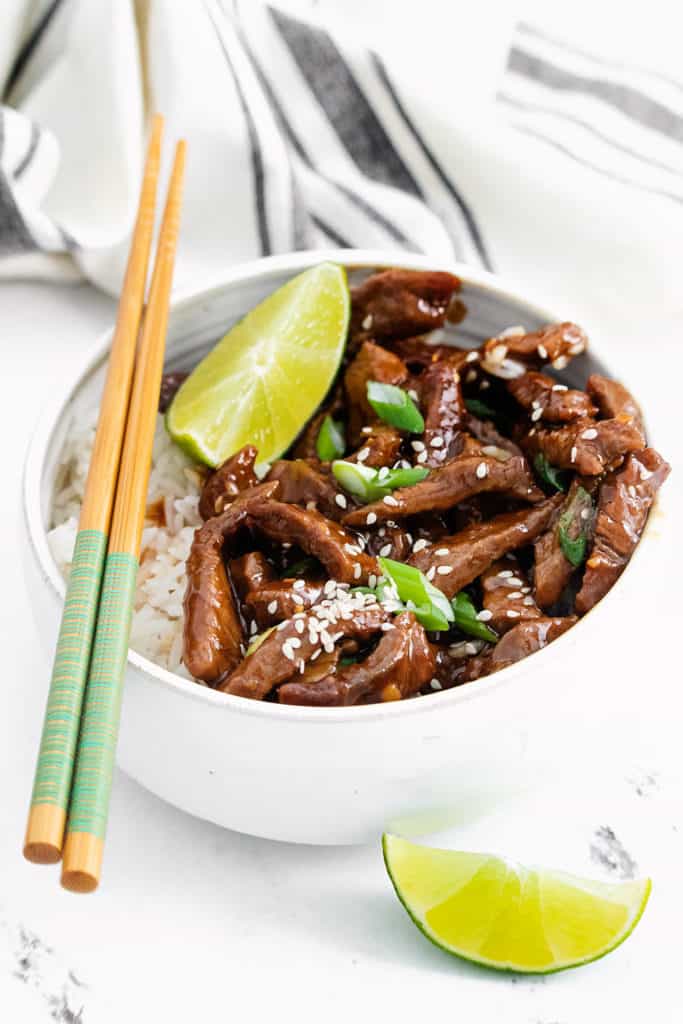 chopsticks resting on white bowl with sesame ginger beef and rice