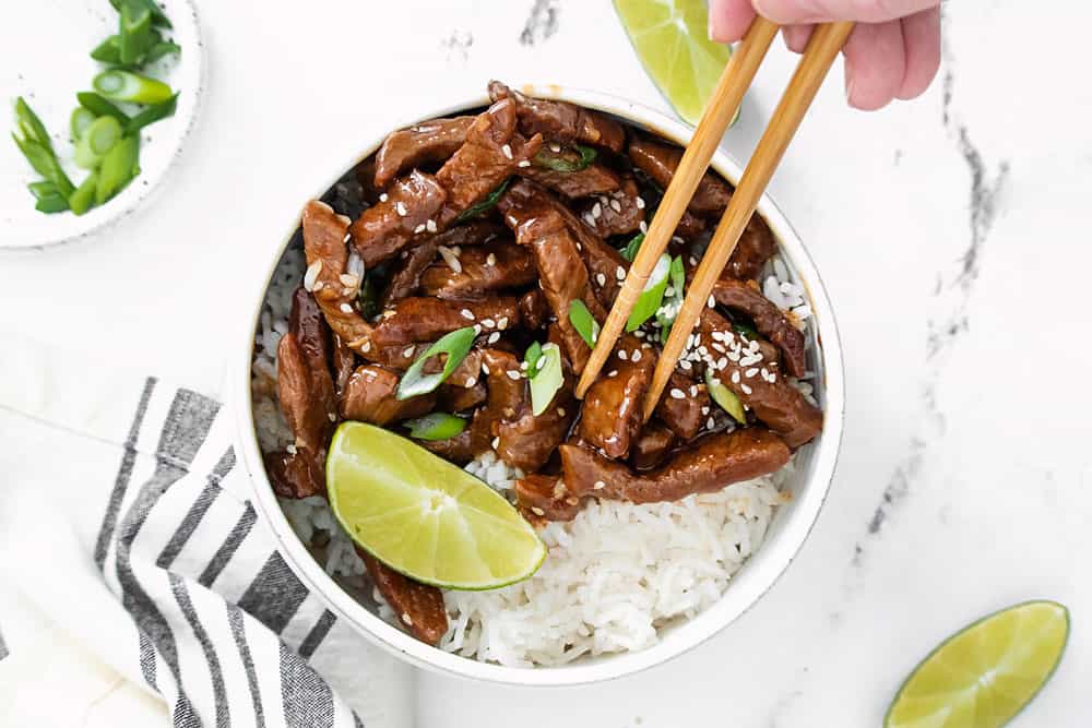 chopsticks picking up piece of sesame ginger beef in bowl