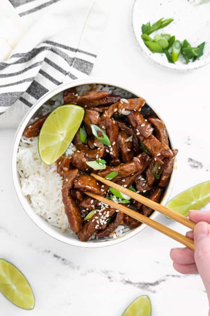 chopsticks eating bowl of sesame ginger beef and rice