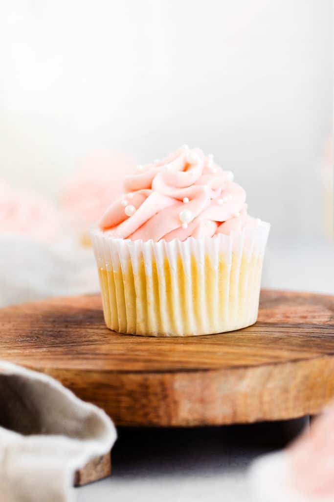 vanilla cupcake topped with swirl of rhubarb buttercream and sprinkles