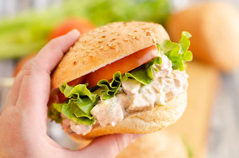 hand holding smoked chicken salad sandwich with lettuce and tomato