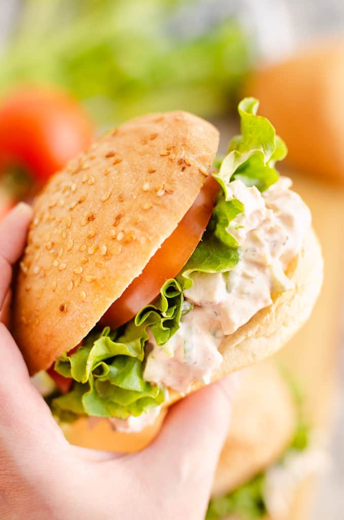 hand holding smoked chicken salad sandwich with lettuce and tomato
