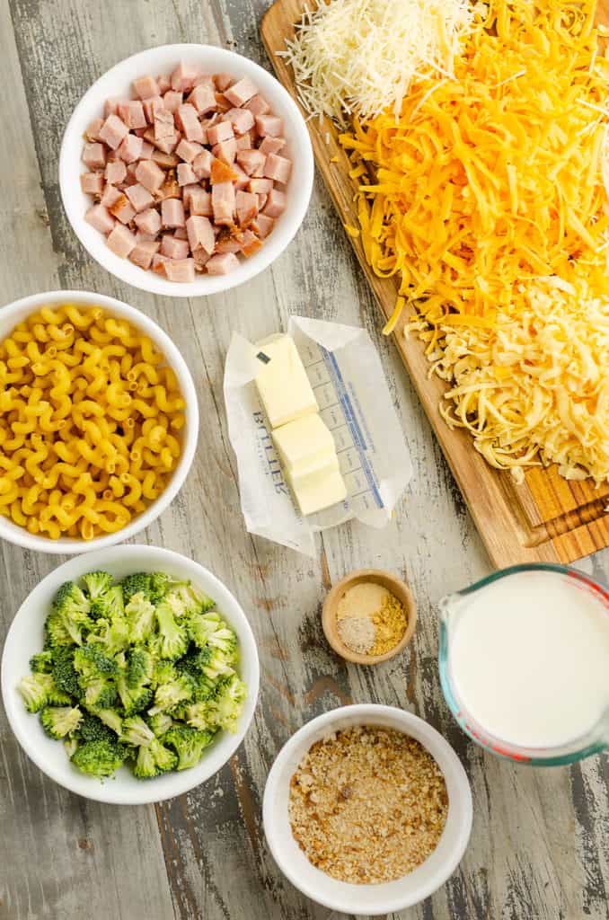 shredded cheese, diced ham, cavatappi pasta noodles, broccoli florets, breadcrumbs, butter, milk and spices on table