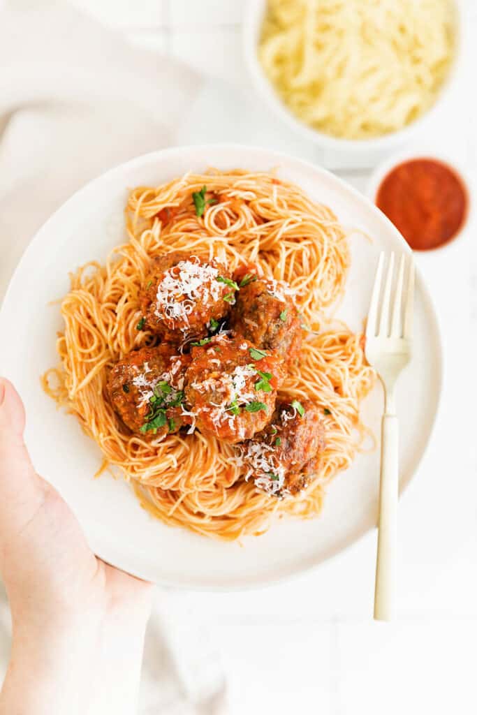 hand hplding plate filled with pasta and air fryer meatballs