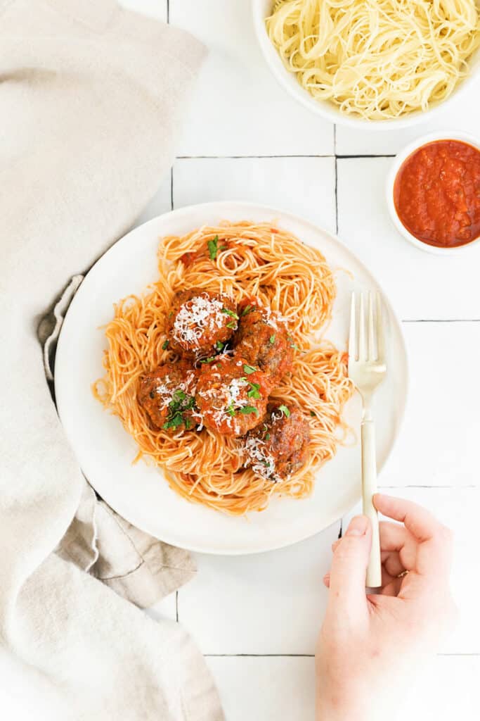 hand holding fork by plate with spaghetti and meatballs