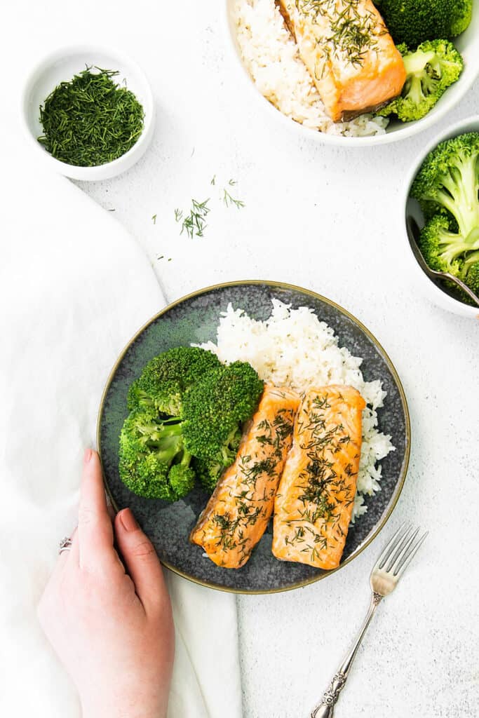 hand holding plate full of salmon rice and broccoli