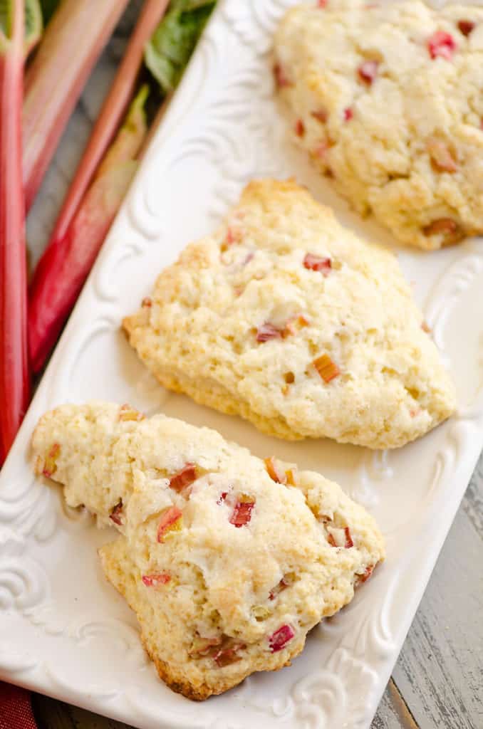 3 rhubarb scones on white platter next to fresh rhubarb stalks