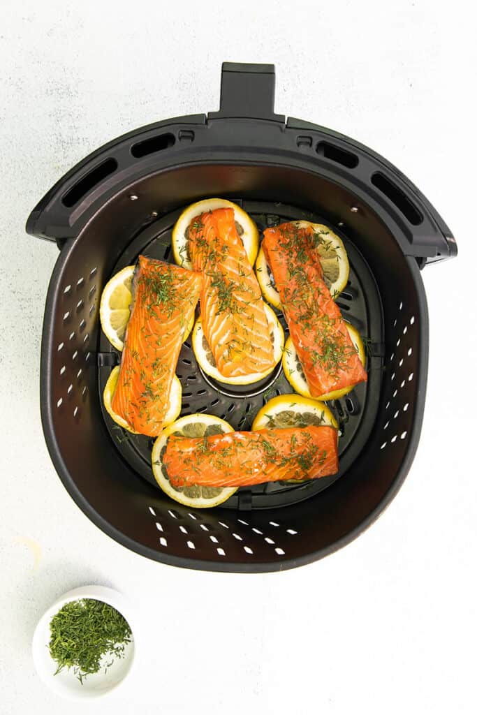 air fryer basket with salmon fillets over lemon slices