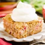 slice of rhubarb cake on white plate topped with whipped cream