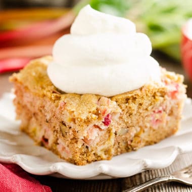 slice of rhubarb cake on white plate topped with whipped cream