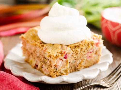 slice of rhubarb cake on white plate topped with whipped cream