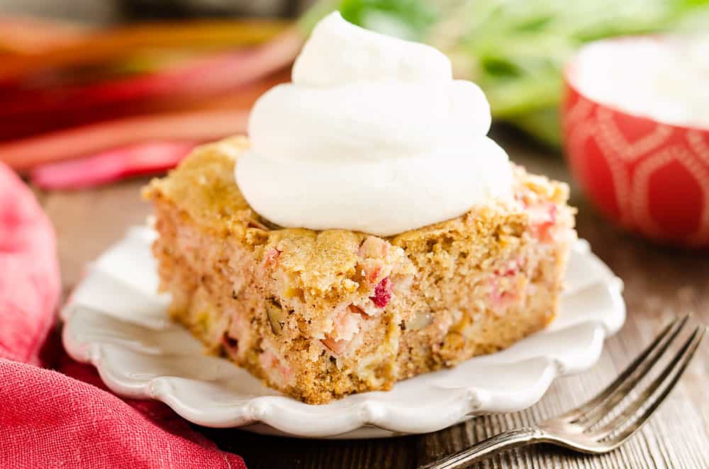 slice of rhubarb cake on white plate topped with whipped cream