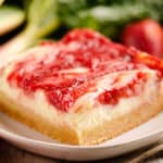 strawberry rhubarb cheesecake bar with sugar cookie crust on plate