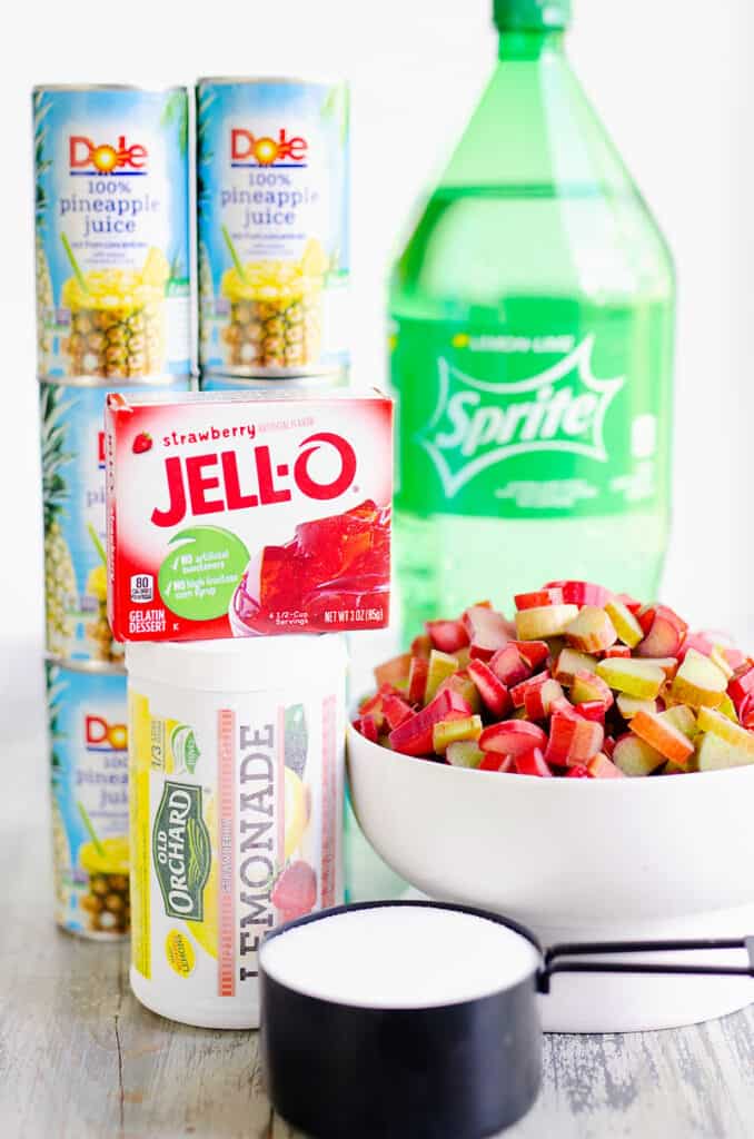 sprite, pineapple juice, strawberry jello, lemonade concentrate, chopped rhubarb and sugar on table