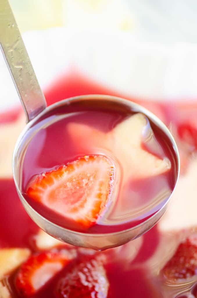 ladle full of strawberry rhubarb punch and fresh strawberries