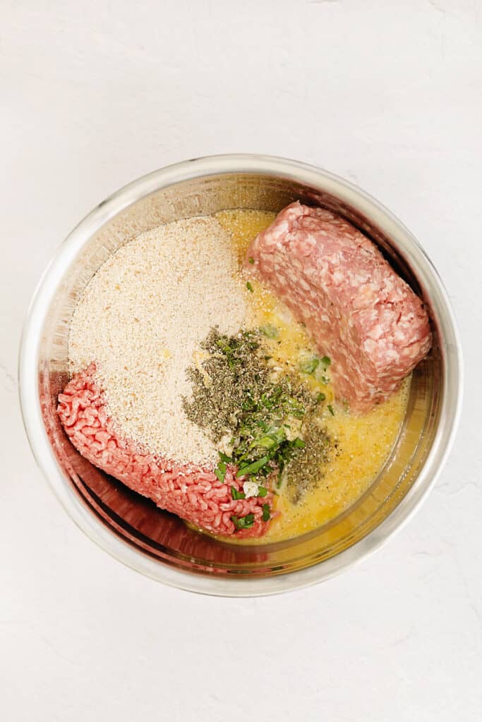 ground beef and pork with meatball ingredients in stainless steel bowl