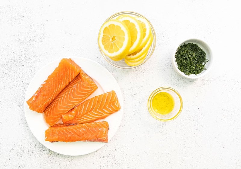 fresh salmon fillets, lemon slices, olive oil and dill on white table