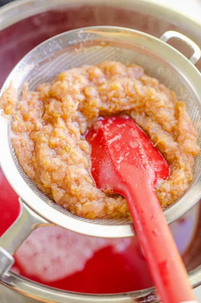 stirring cooked rhubarb in mesh strainer over bowl