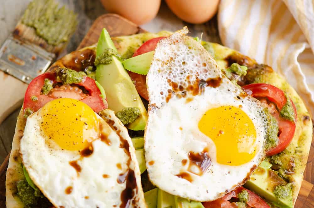 breakfast caprese flatbread topped with balsamic glaze on table with eggs