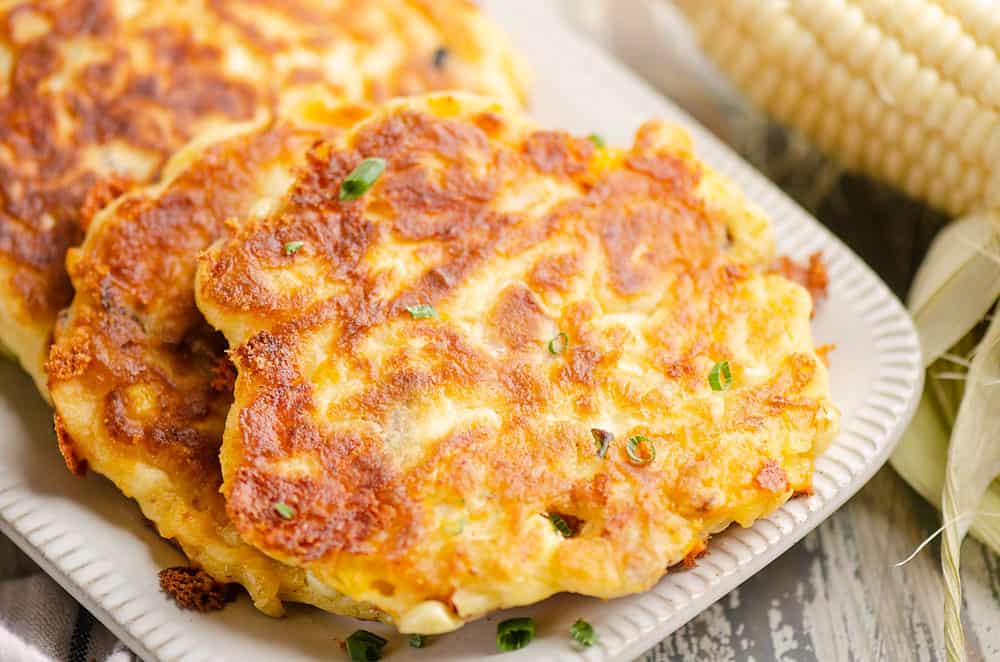 sweet corn fritters on white platter next to sweet corn