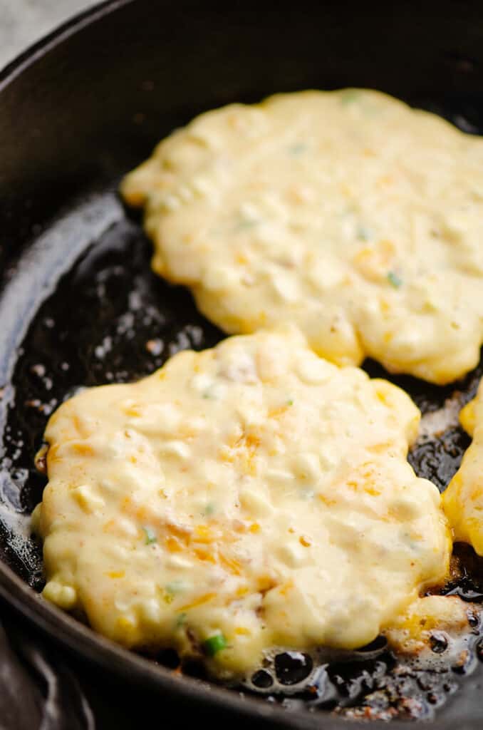 cheesy corn fritter cooking in cast iron skillet with olive oil