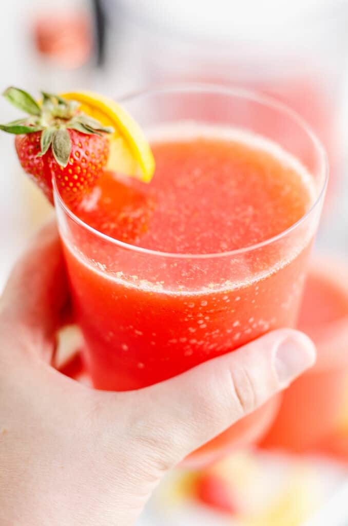 glass of frozen strawberry vodka lemonade with slice of lemon in hand