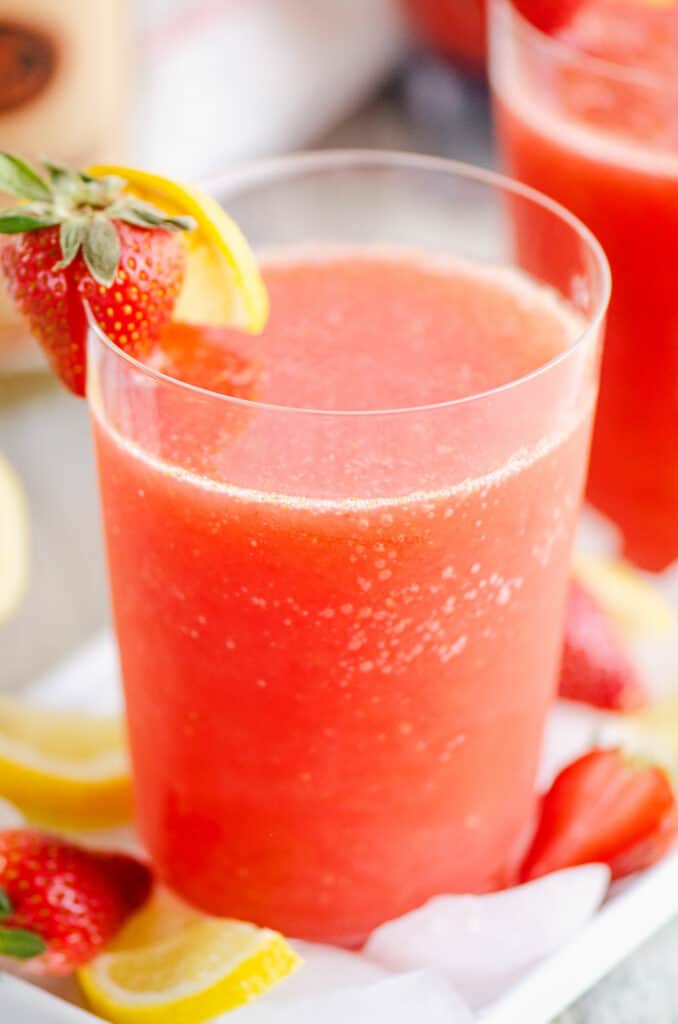 glass of frozen strawberry vodka lemonade on table with ice and lemon