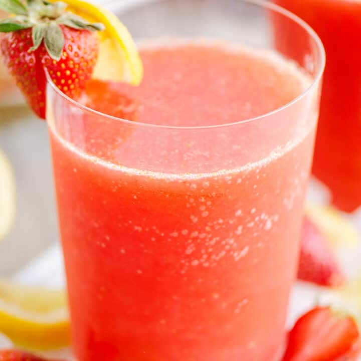 glass of frozen strawberry vodka lemonade on table with ice and lemon