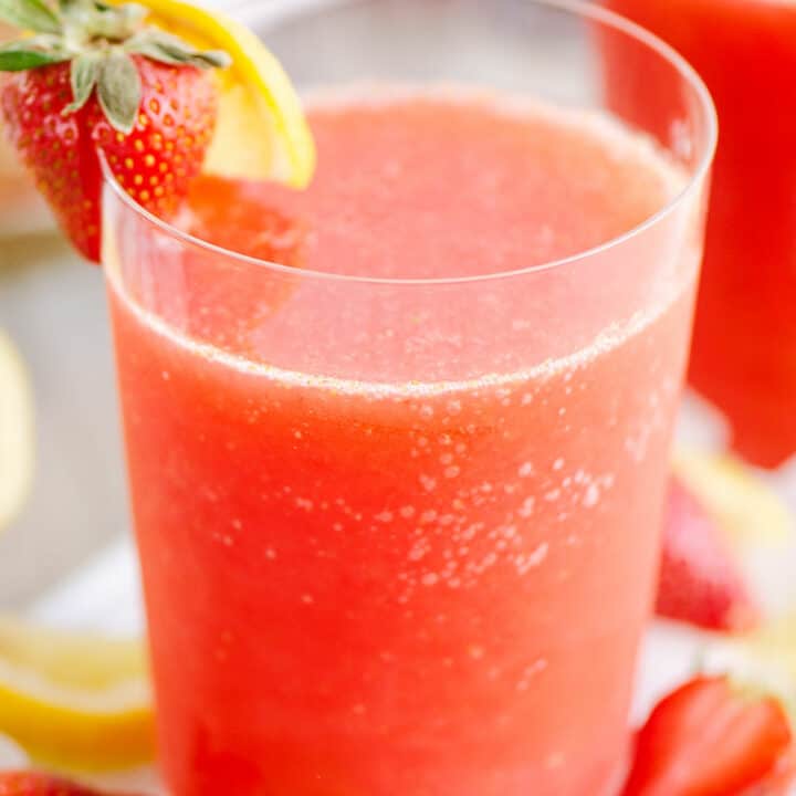 glass of frozen strawberry vodka lemonade on table with ice and lemon