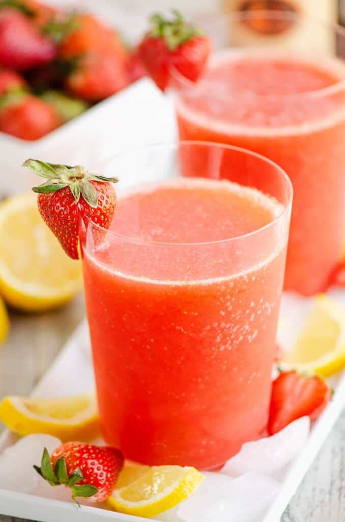 glass of frozen strawberry vodka lemonade on tray of ice with lemons
