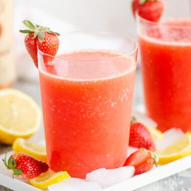 glasses of frozen strawberry vodka lemonade on table with bottle of alcohol and fruit