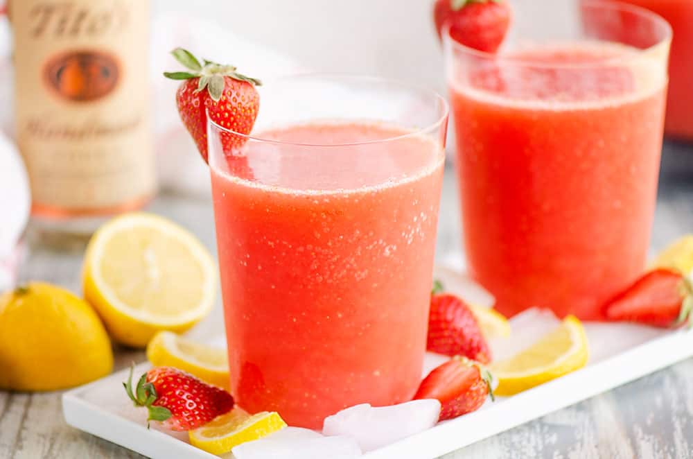 glasses of frozen strawberry vodka lemonade on table with bottle of alcohol and fruit