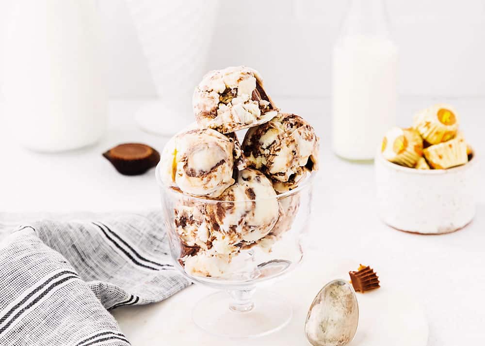 Moose tracks ice cream scoops in glass bowl on table with reese's peanut butter cups