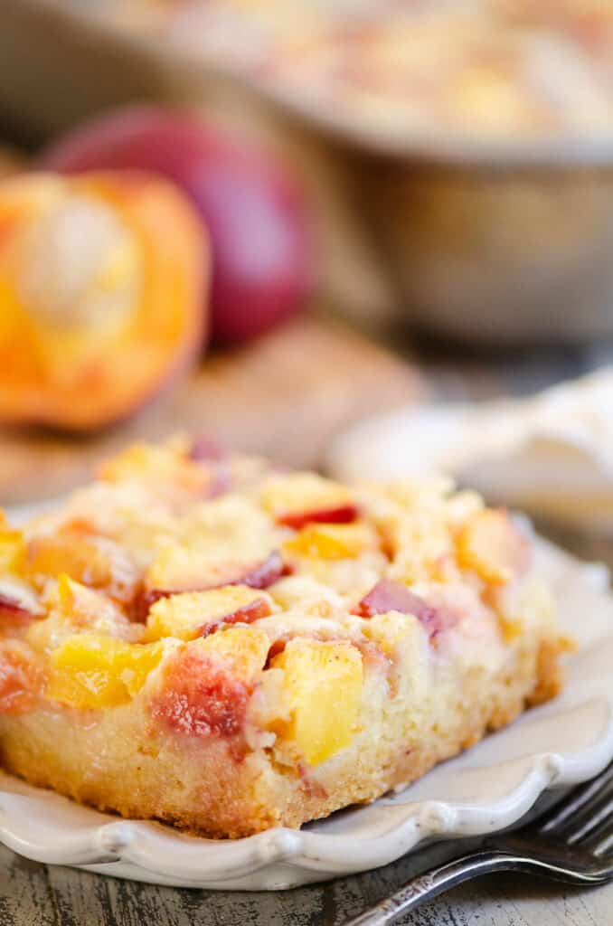 side of slice of peach custard dessert on plate with fresh peaches