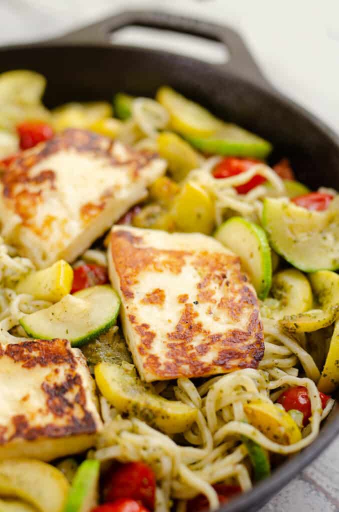 grilled halloumi cheese over vegetables and pesto spaghetti