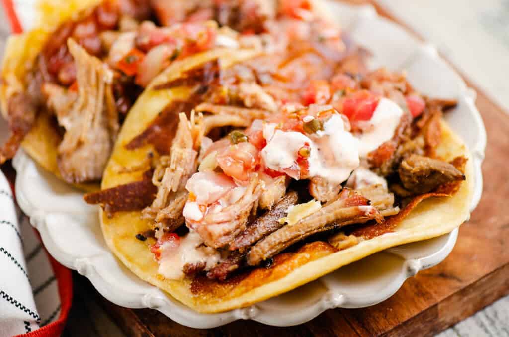 crispy cheese and pork carnitas in flour tortillas on white scalloped plate