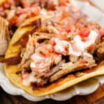 crispy cheese and pork carnitas in flour tortillas on white scalloped plate