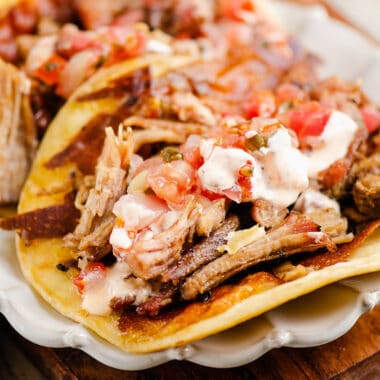 crispy cheese and pork carnitas in flour tortillas on white scalloped plate