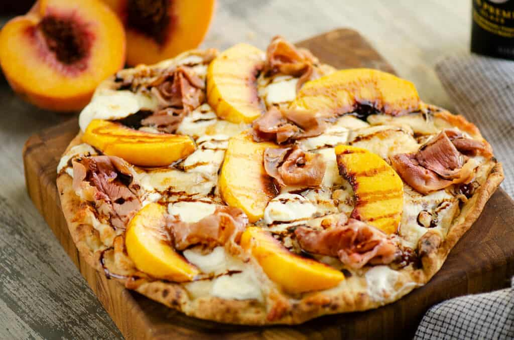 peach and prosciutto pizza with balsamic glaze on cutting board