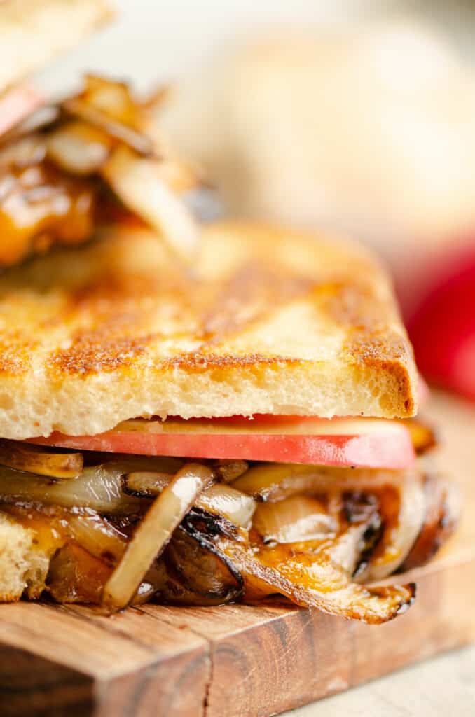 Half of grilled cheese with apples and onions on cutting board