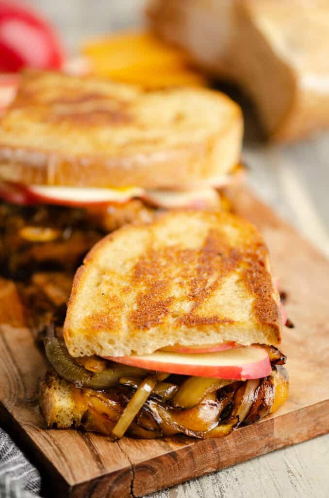 cutting board with halves of grilled cheese with apples and onions
