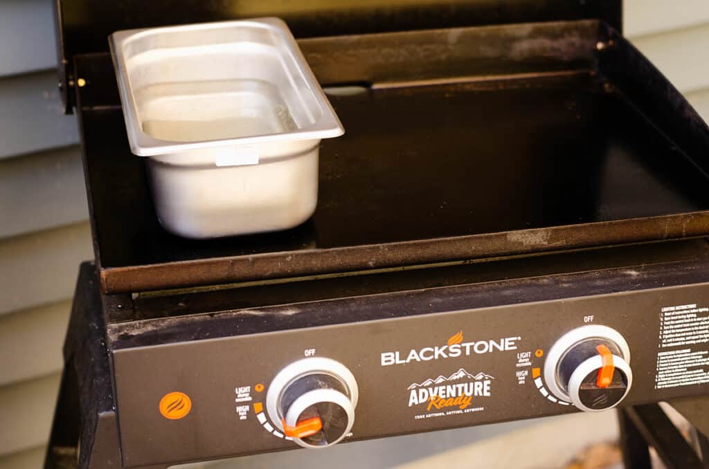 Blackstone griddle with hotel pan full of boiling water to cook pasta