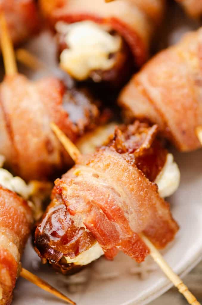 bacon wrapped dates skewered with toothpicks on white plate
