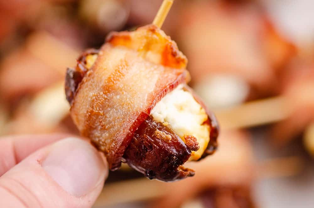 fingers holding bacon wrapped goat cheese date