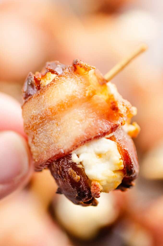 fingers holding bacon wrapped goat cheese stuffed date