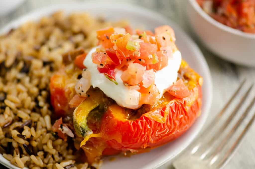 taco stuffed pepper topped with sour cream and pico on plate with rice