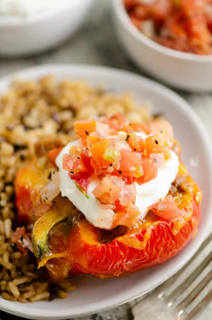 cheesy taco stuffed pepper topped with sour cream and pico on plate with rice