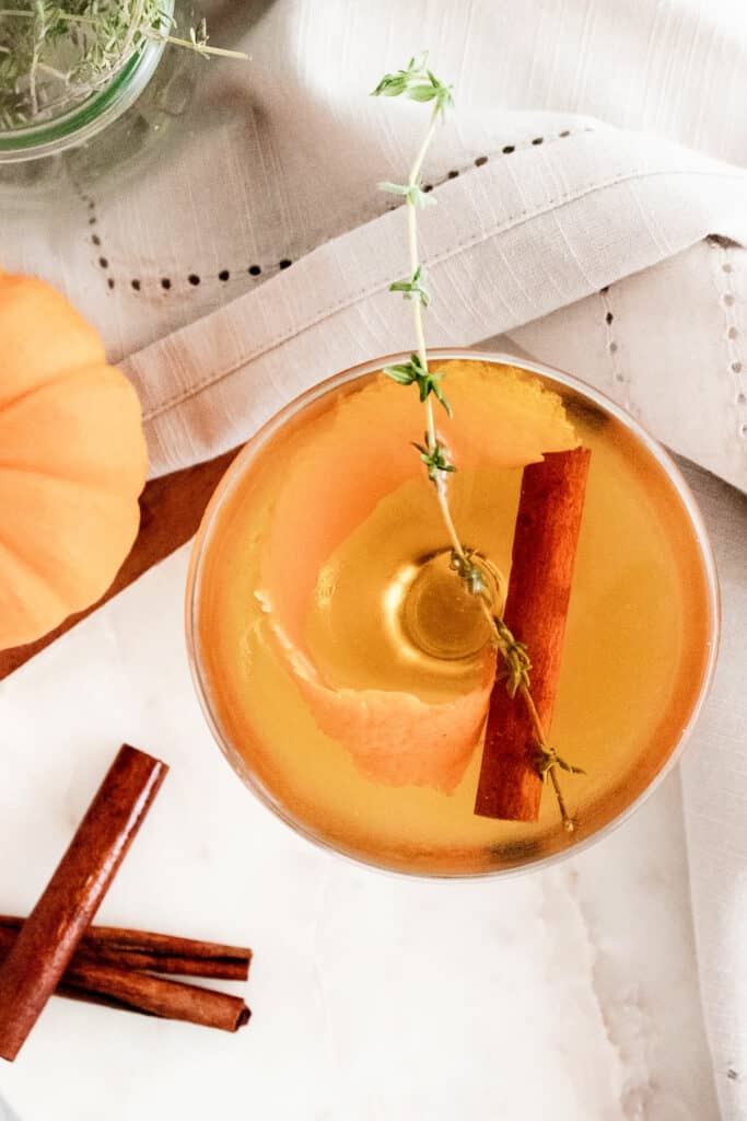 fall spiced old fashioned with cinnamon stick and thyme sprig in glass on white table