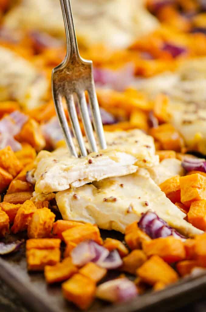 honey mustard chicken with fork and sweet potatoes on sheet pan